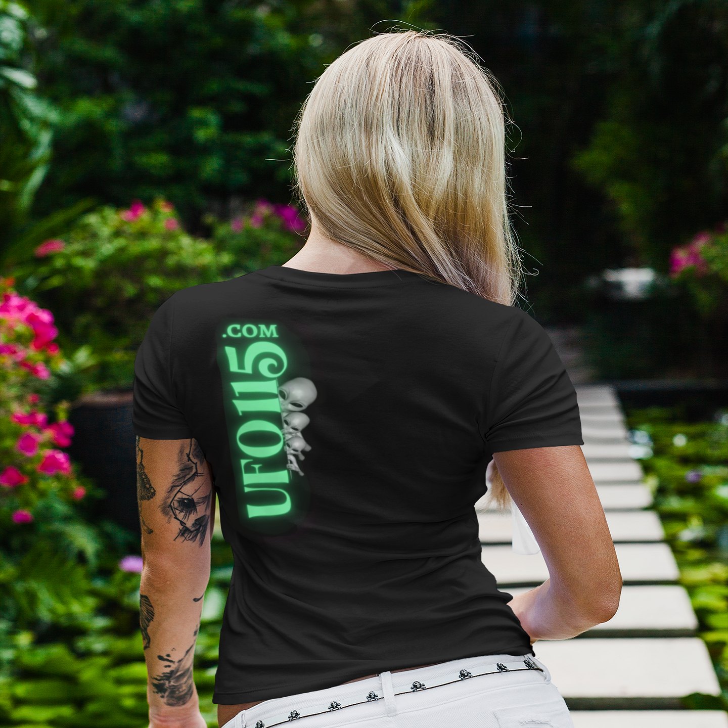 Already Here Neon Grey T-shirt in Black, back print, worn by a model (tropical garden walkway (back)). AI-edited photo: the real print artwork was digitally placed on a model photo.